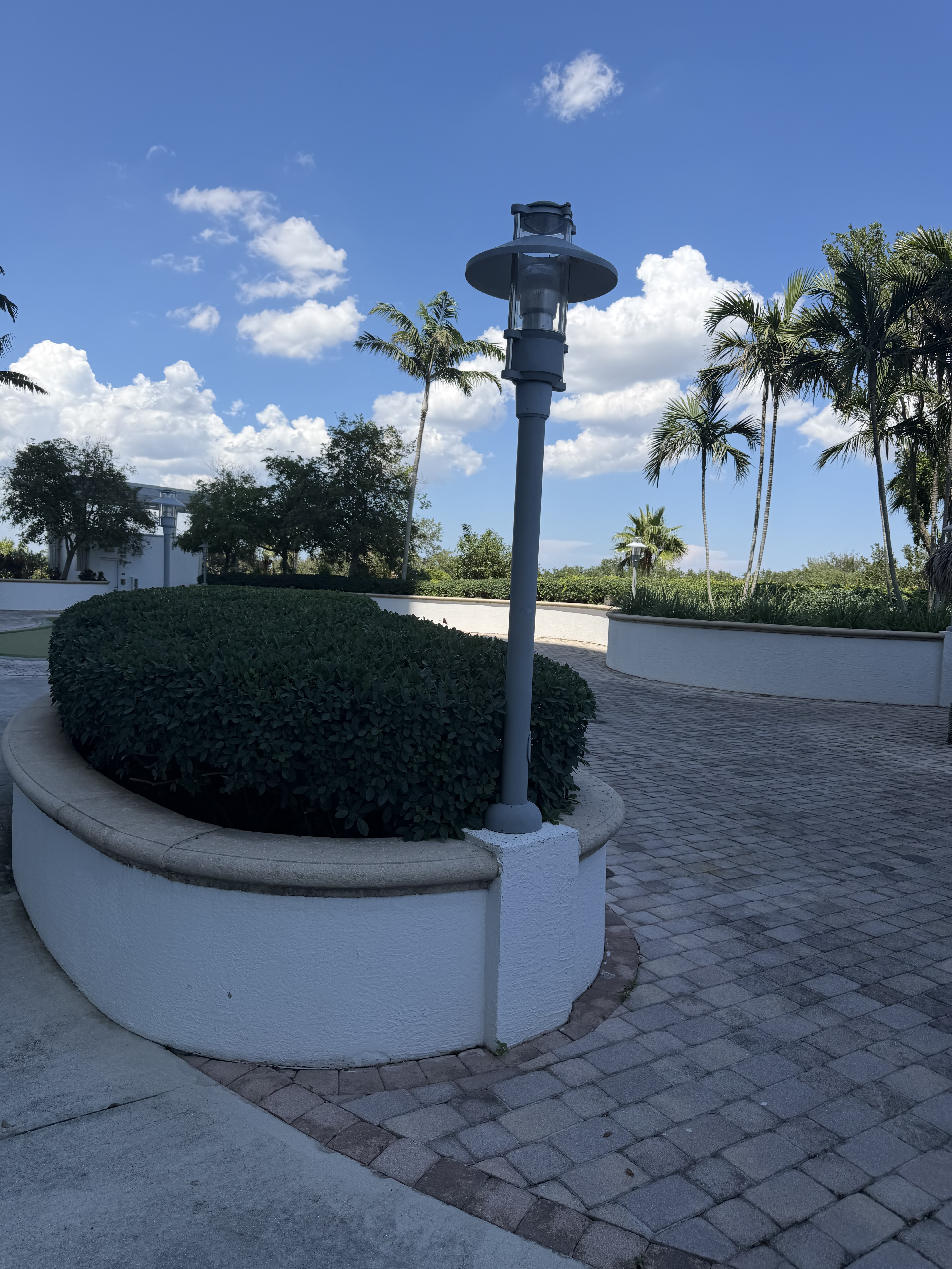 The entry court today — a faded grey lantern-style single-head garden lamp atop a circular planter pedestal, chalky powder coat showing its age.