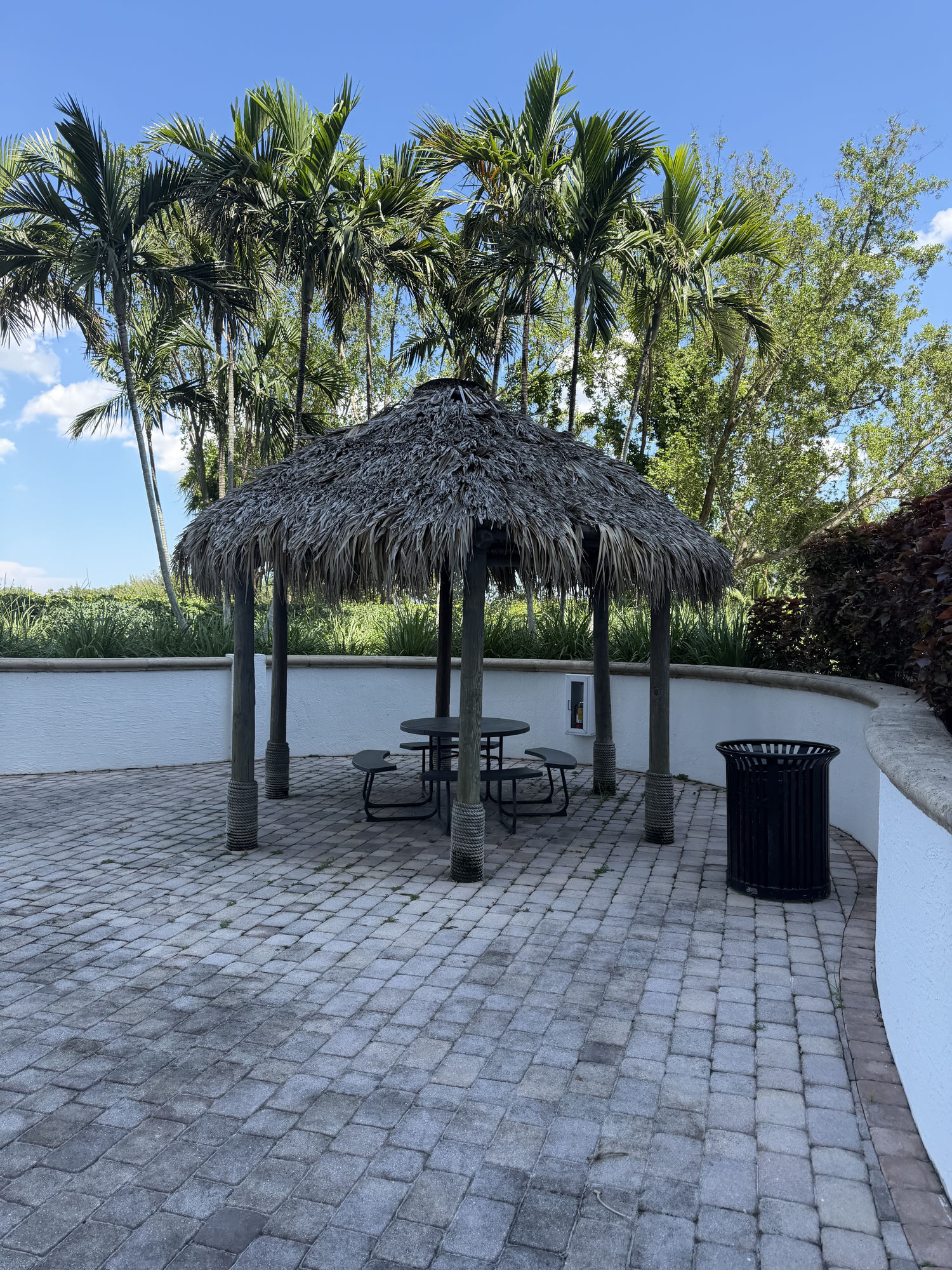 The 4th floor lobby patio today — a weathered thatched tiki hut over the picnic table, with a dated black slatted trash can off to the right.